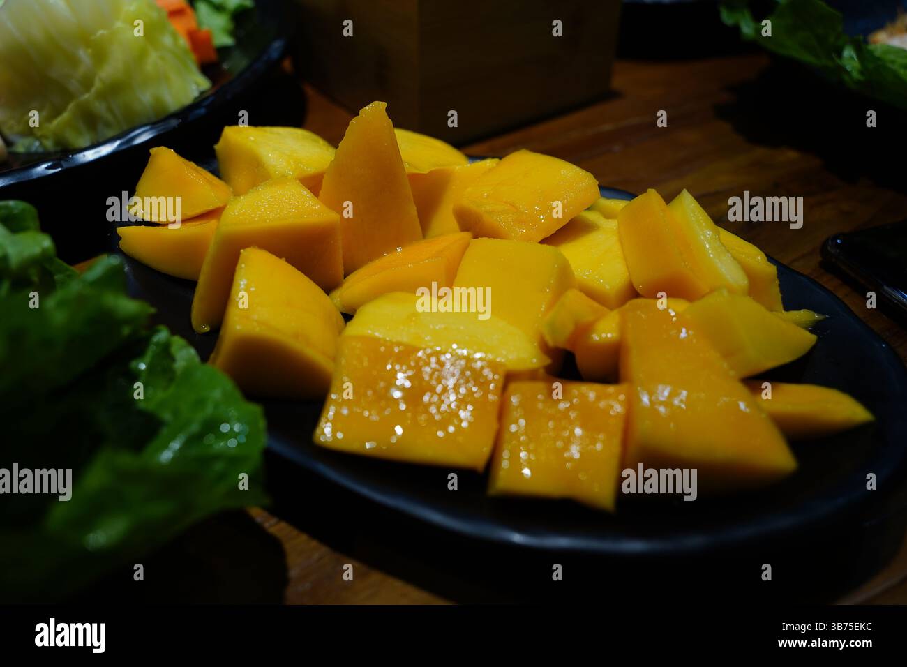 Gros plan de mangue fraîche en cubes et de fruits du dragon sur une assiette sombre – plateau de fruits tropicaux Banque D'Images