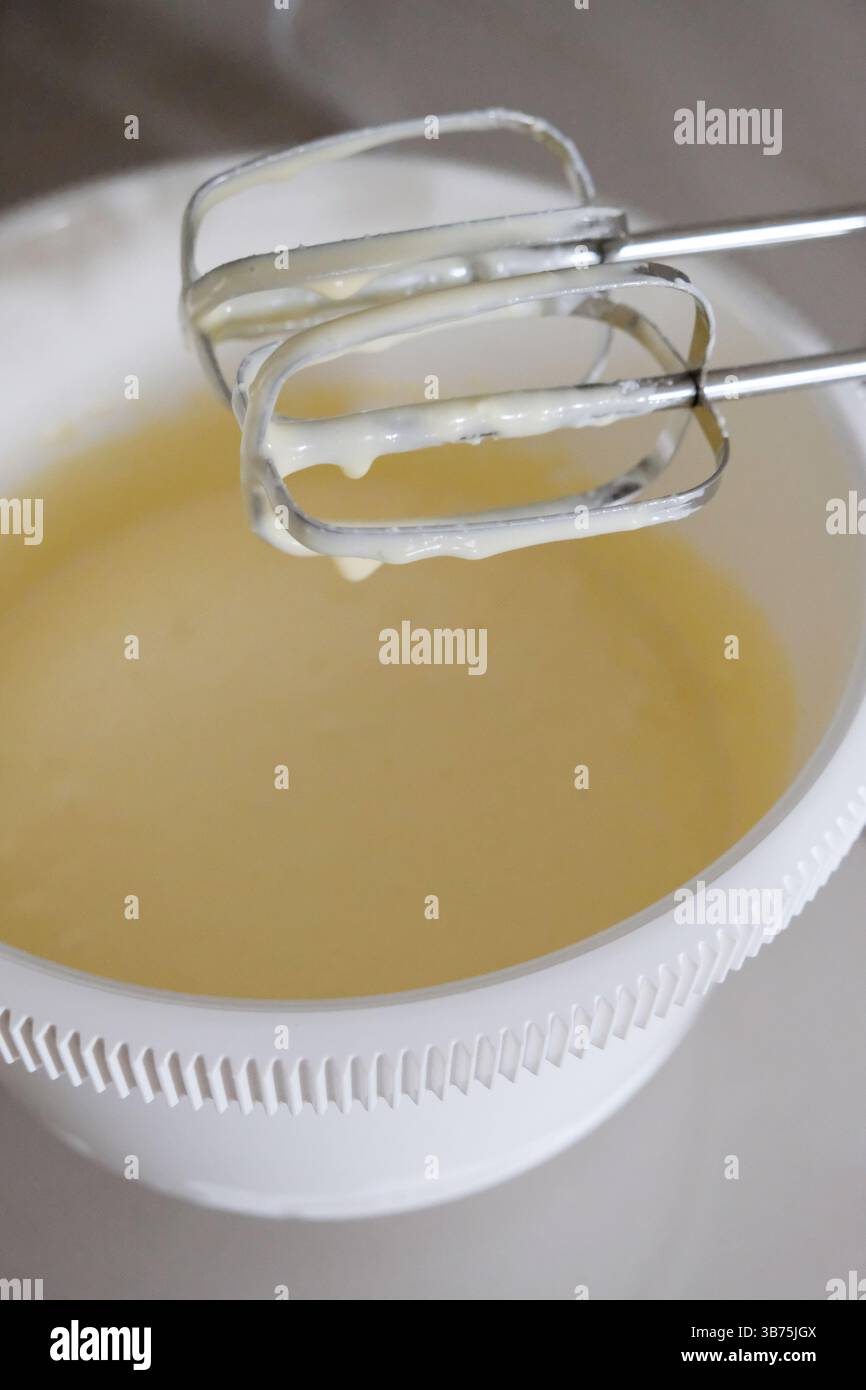 Préparation du mélange de pâte sur un bol avec mélangeur mobile, oeufs, lait, pâte, eau, ingrédients en mélange, vue rapprochée, activité culinaire. Banque D'Images