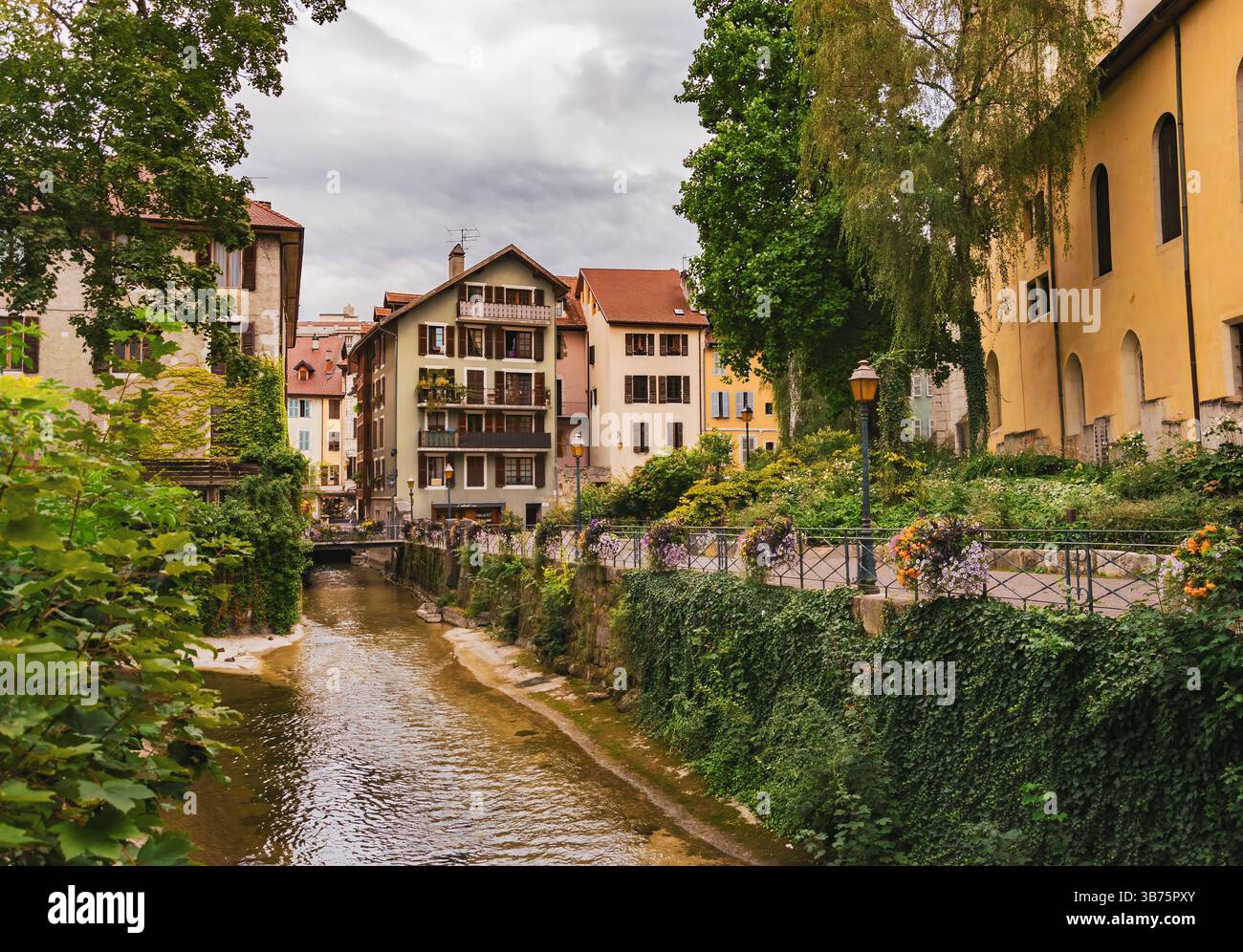 Balustrades florales sur un canal étroit, encadrées par de vieux murs de pierre et des reflets colorés dans la lumière tranquille du matin Banque D'Images