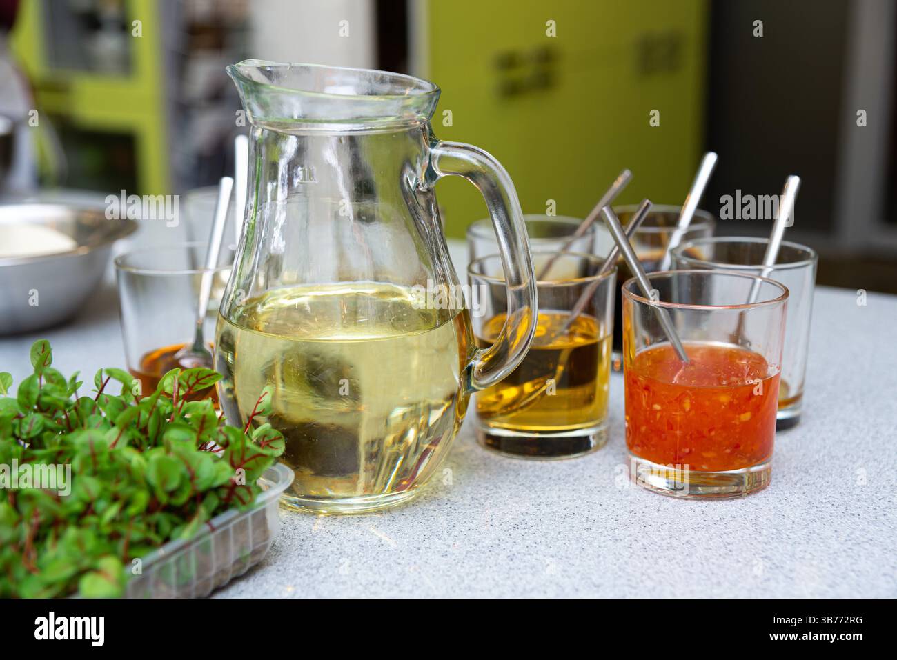 Une sélection de sauces dans des tasses en verre, y compris des liquides jaunes, oranges et clairs, avec des herbes fraîches au premier plan sur un comptoir de cuisine. Banque D'Images