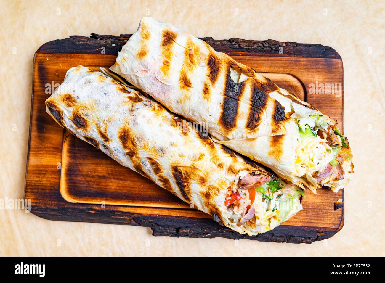 Deux wraps grillés remplis d'ingrédients assortis sont présentés sur un plateau en bois. Les wraps présentent un mélange de viandes et de légumes frais, inviti Banque D'Images