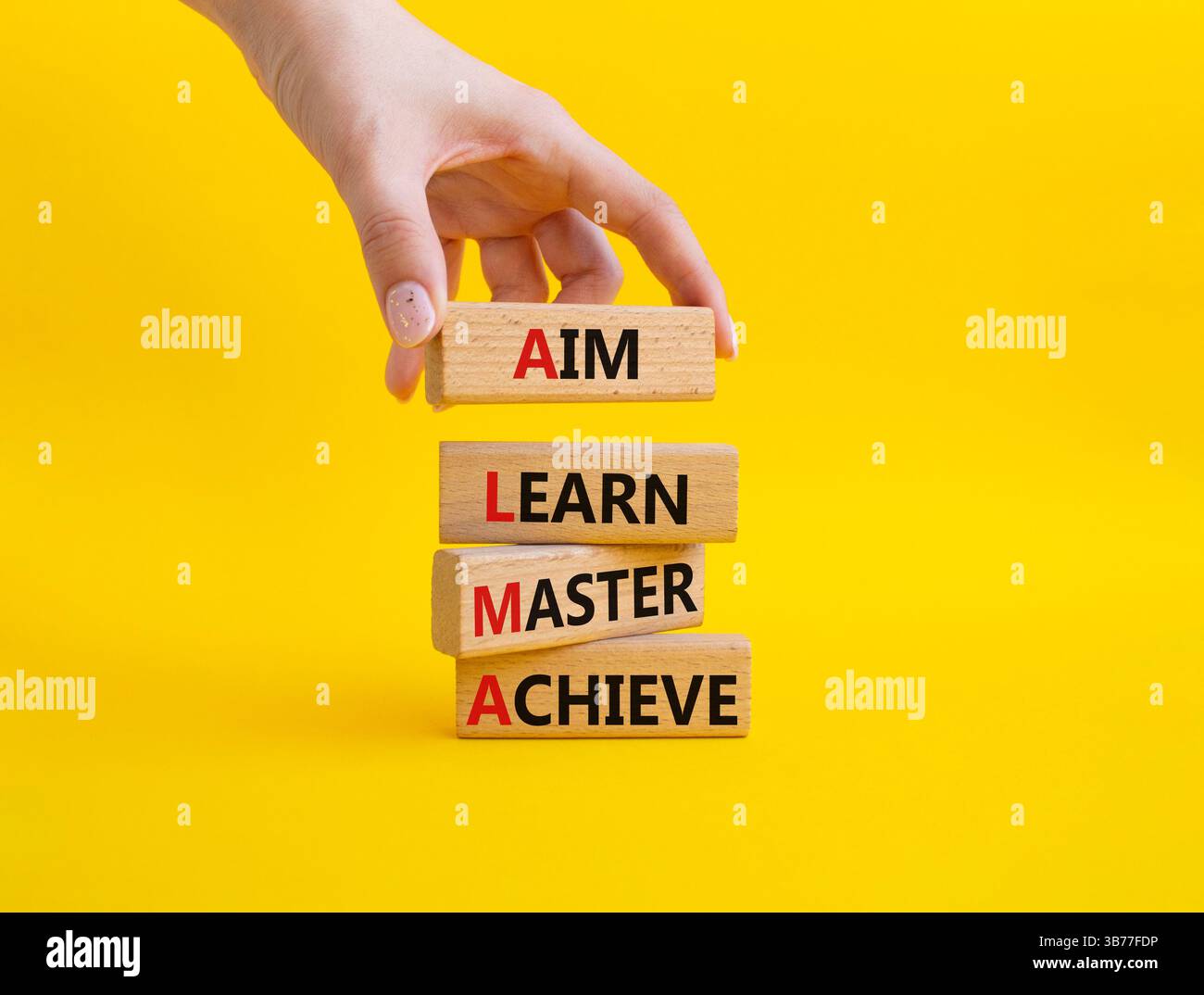 Symbole AIM apprendre Maître réaliser. Mot concept AIM apprendre Master Achieve sur des blocs de bois. Beau fond jaune. Main d'homme d'affaires. Affaires et A Banque D'Images