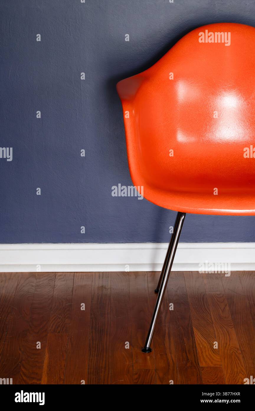 Une chaise en fibre de verre orange de style moderne dans une chambre avec un mur bleu foncé et parquet Banque D'Images