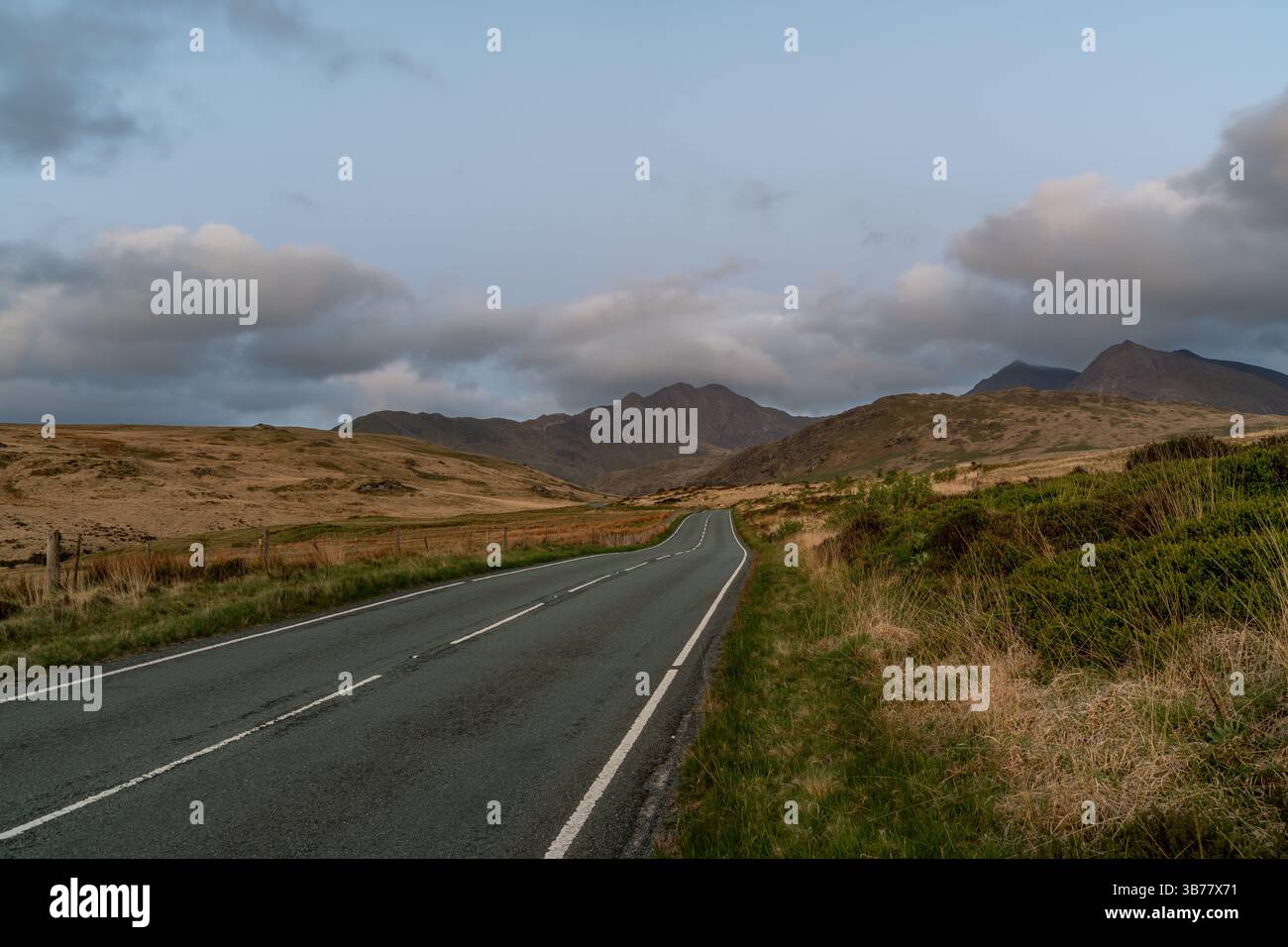 Route sinueuse s'étend au loin, menant aux majestueuses montagnes de Snowdonia sous un ciel nuageux nocturne, entouré par la beauté naturelle Banque D'Images
