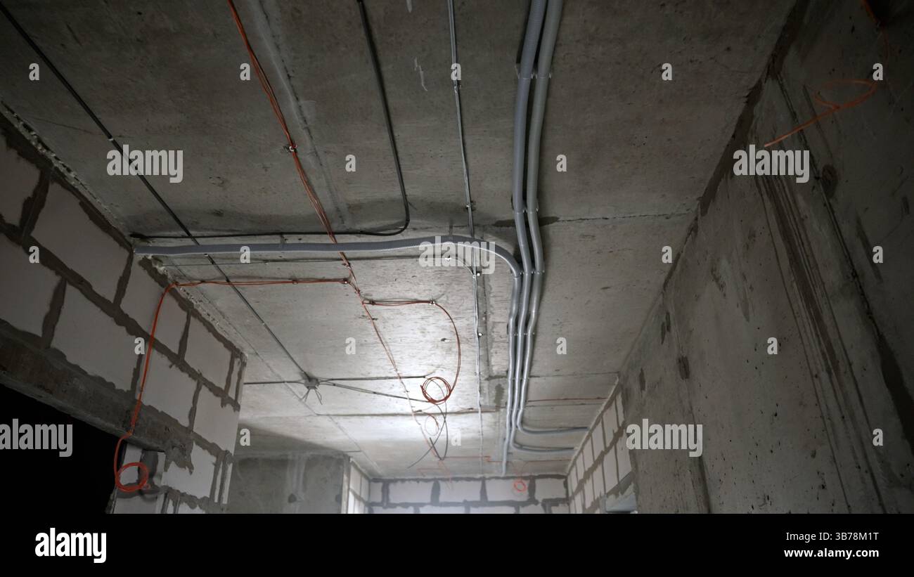 Intérieur sombre du chantier de construction montrant des conduites électriques montées sur un plafond en béton au-dessus de murs de briques blanches dans un bâtiment résidentiel sous Ren Banque D'Images