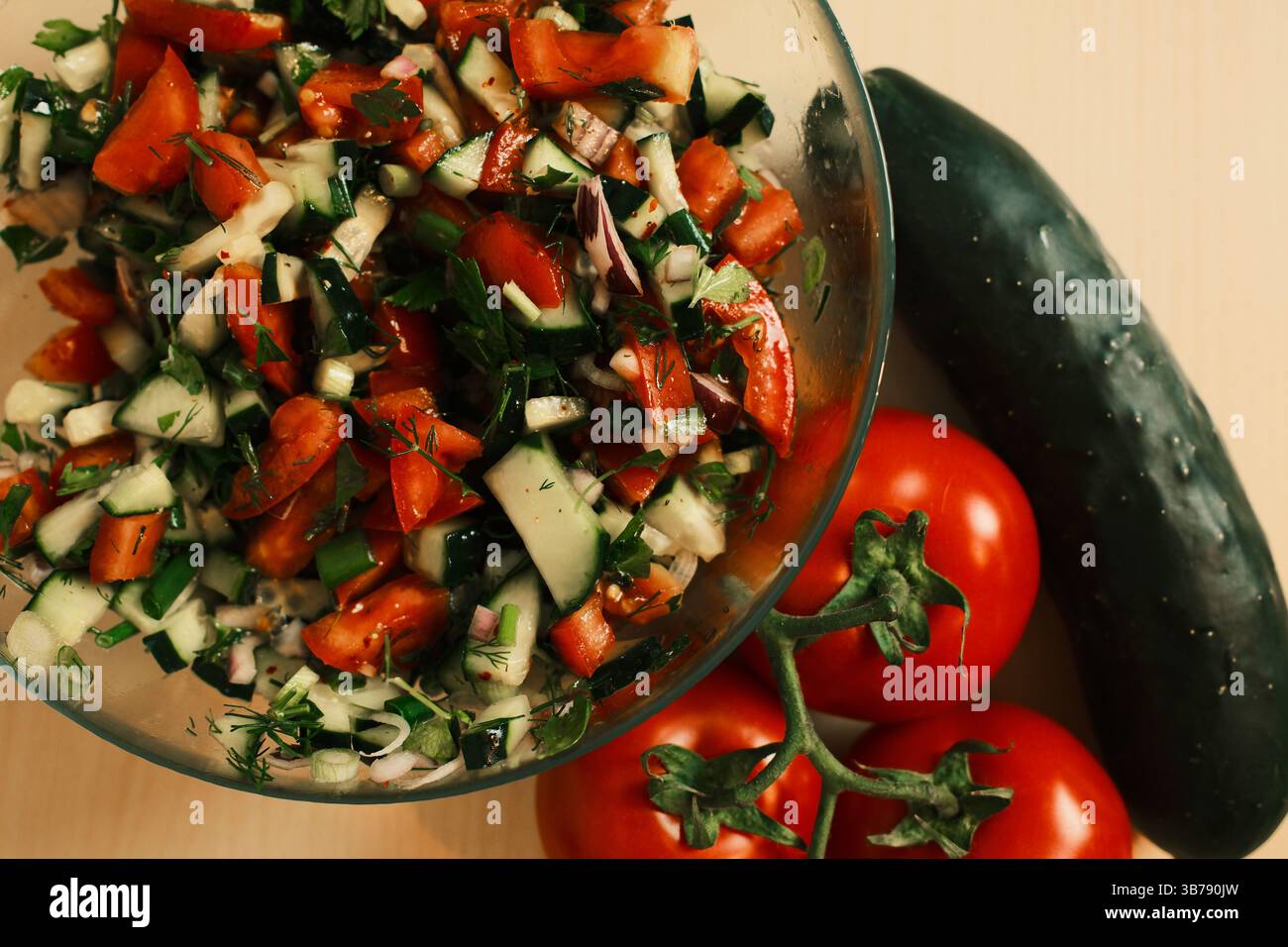 Salade de tomates et de concombre hachées avec oignon rouge, persil, aneth et oignons verts dans un bol en verre, mettant en valeur des légumes frais et colorés prêts pour un h. Banque D'Images