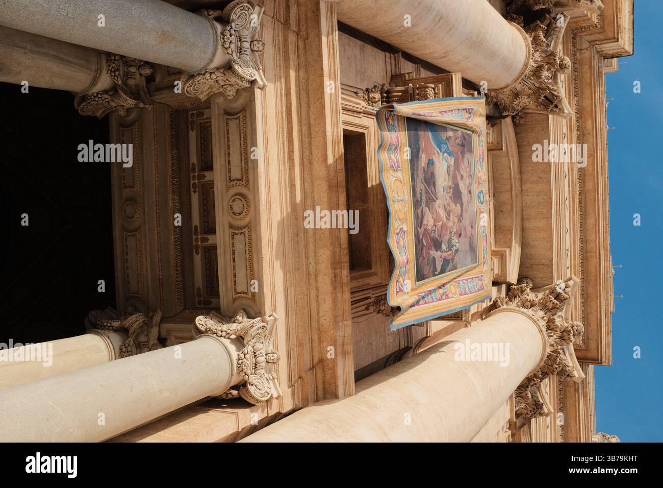 Bannière tapisserie accrochée aux colonnes de la façade de la basilique Saint-Pierre dans la Cité du Vatican pour un événement religieux spécial ou une bénédiction papale sous le ciel bleu. Photo de haute qualité Banque D'Images