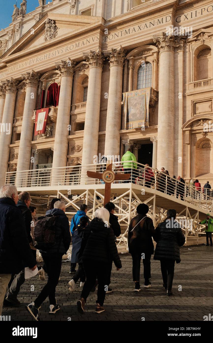 Pèlerins et touristes entrant dans la porte sainte de la basilique Saint-Pierre dans la Cité du Vatican par des portes en bronze ornées pendant le Jubilé de l'année Sainte avec croix visible et rassemblement spirituel sur le site catholique sacré. Photo de haute qualité Banque D'Images