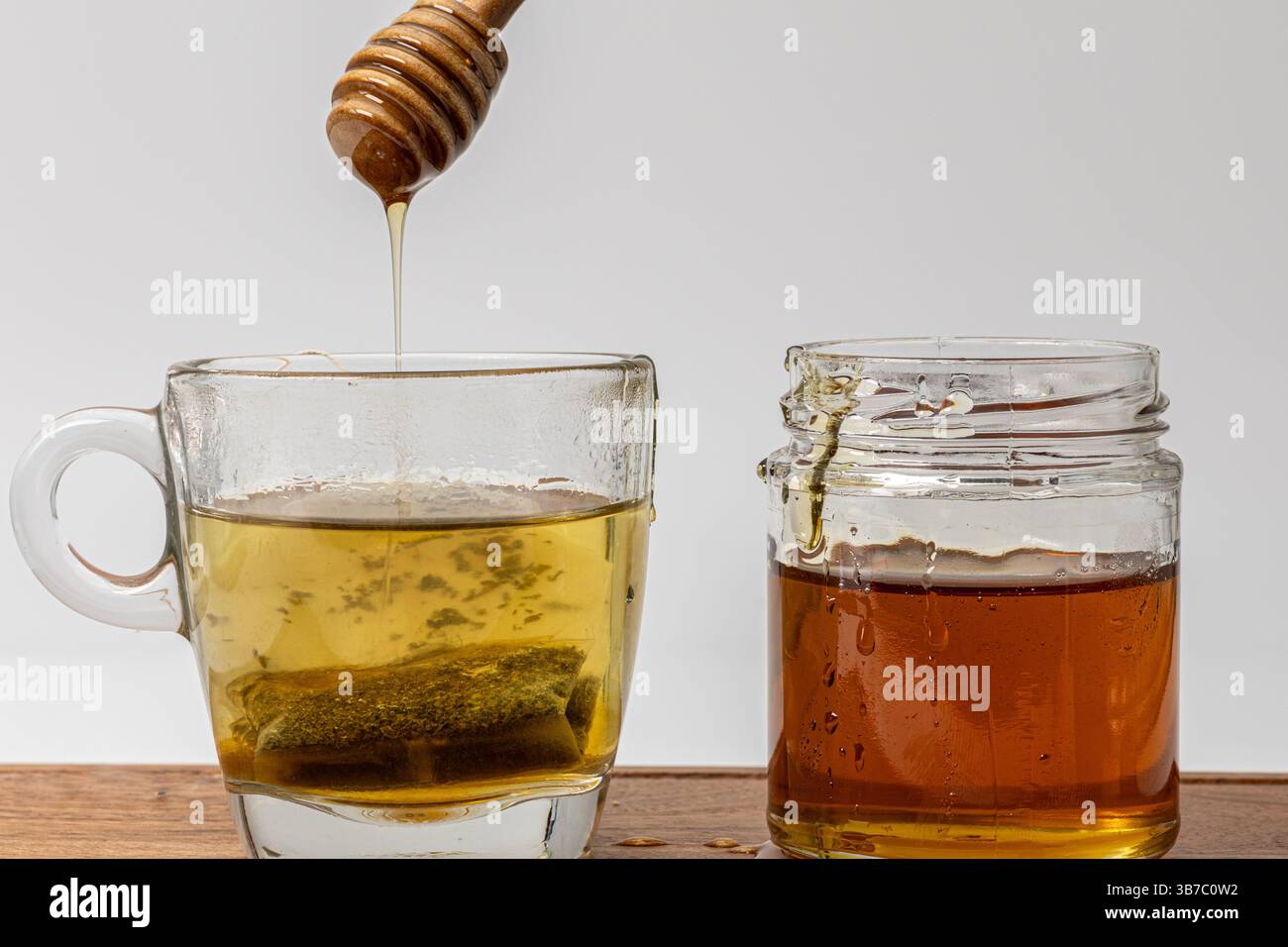 Miel qui coule d'une benne dans une tasse de thé vert conservé à côté d'un pot de miel Banque D'Images