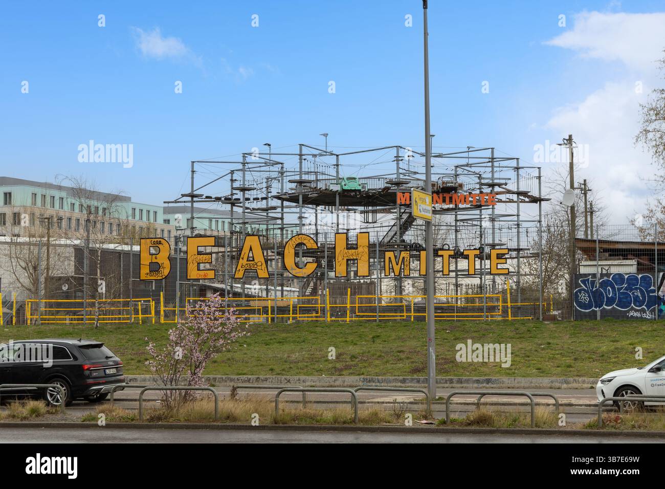 Scène urbaine à Berlin avec le lettrage « BEACH MITTE » sur une structure, avec des voitures garées le long d'une rue humide. Allemagne. Berlin, Allemagne. 30 mars 2025. Banque D'Images