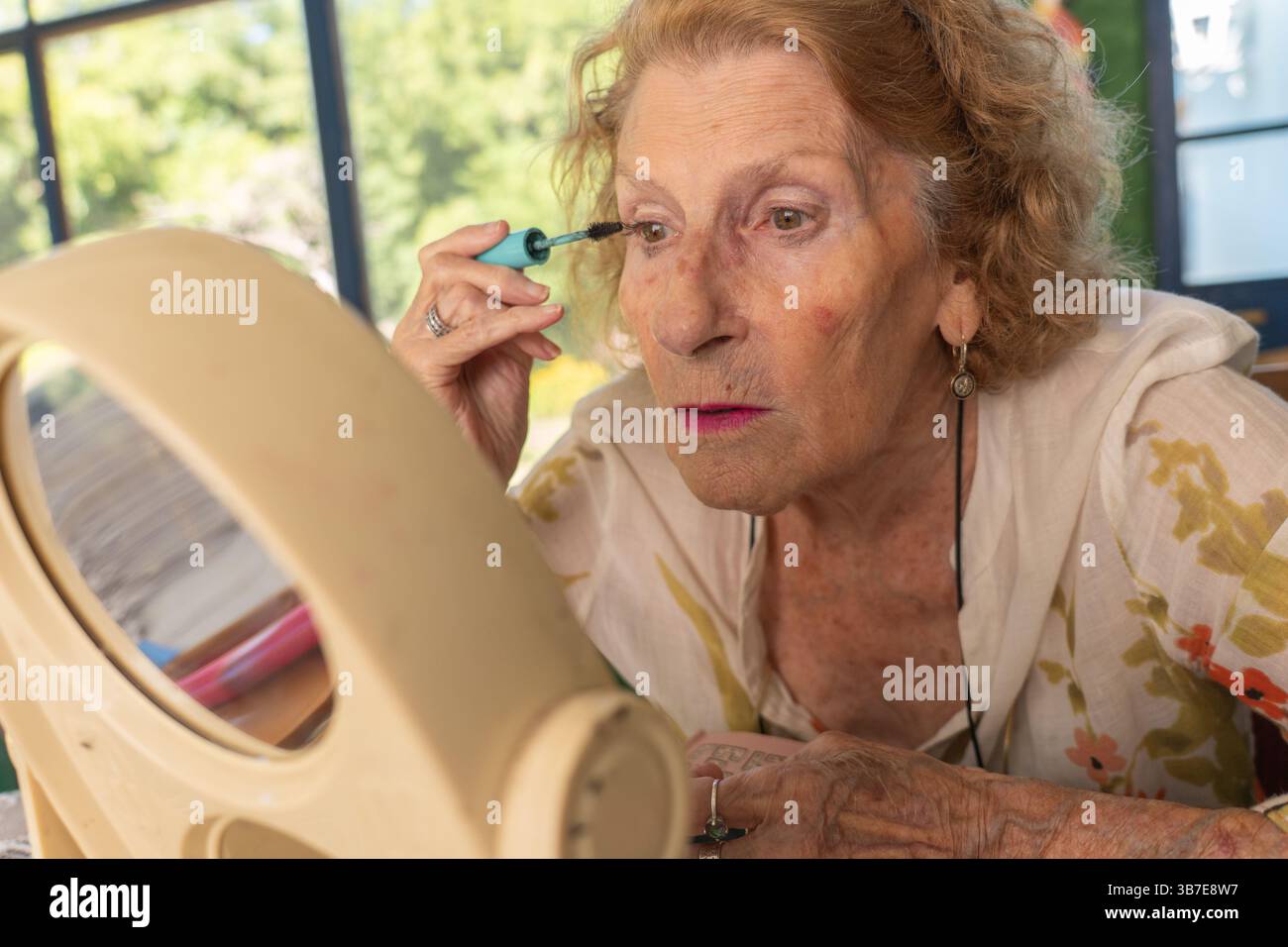 Femme senior appliquant le mascara tout en regardant dans un miroir, se préparant à une sortie. Embrassant sa routine beauté, elle apprécie un moment de soins personnels et Banque D'Images