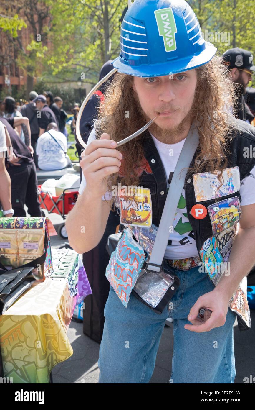Un homme aux cheveux longs et un casque vaporise utilisant un inhalateur DNVP DynaVap. Au Washington Square Park à Manhattan le 20/04/25. Banque D'Images