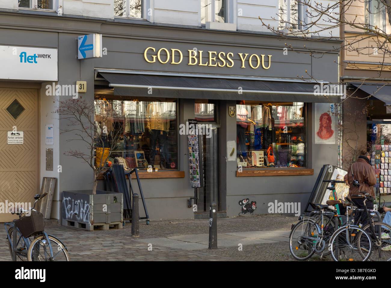 StoreFront à Berlin avec le panneau « DIEU VOUS BÉNISSE » au-dessus de l'entrée, entouré de vélos et de piétons, mettant en valeur une scène de rue urbaine dynamique Banque D'Images