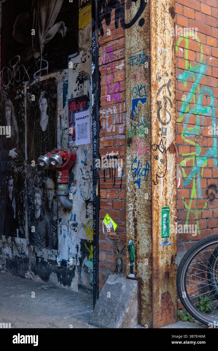 Ruelle urbaine avec art de rue, graffiti, colonne en métal rouillé, affiches et roue de vélo. Un aperçu brut et artistique de la culture de rue gravissime de Berlin. Banque D'Images