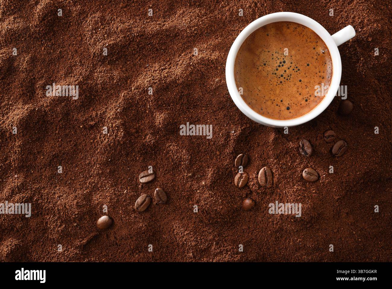 Tasse à café en céramique blanche remplie de café mousseux sur un côté sur un fond de café moulu et de grains autour. Vue de dessus. Banque D'Images