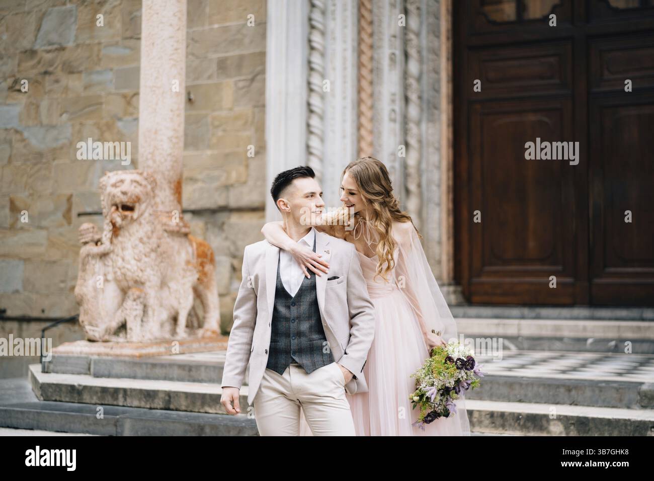 Mariée avec un bouquet de fleurs embrasse les épaules de marié souriant sur les marches à l'entrée de la basilique de Santa Maria Maggiore à Rome. Banque D'Images