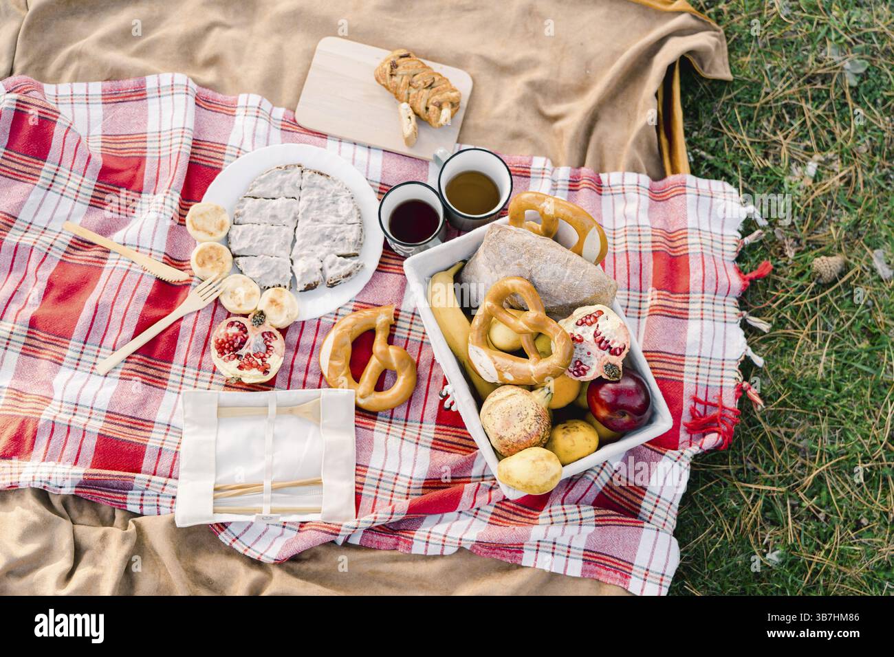 Tasses de café debout sur une couverture à côté des petits pains et des fruits dans un panier et une tarte tranchée. Banque D'Images
