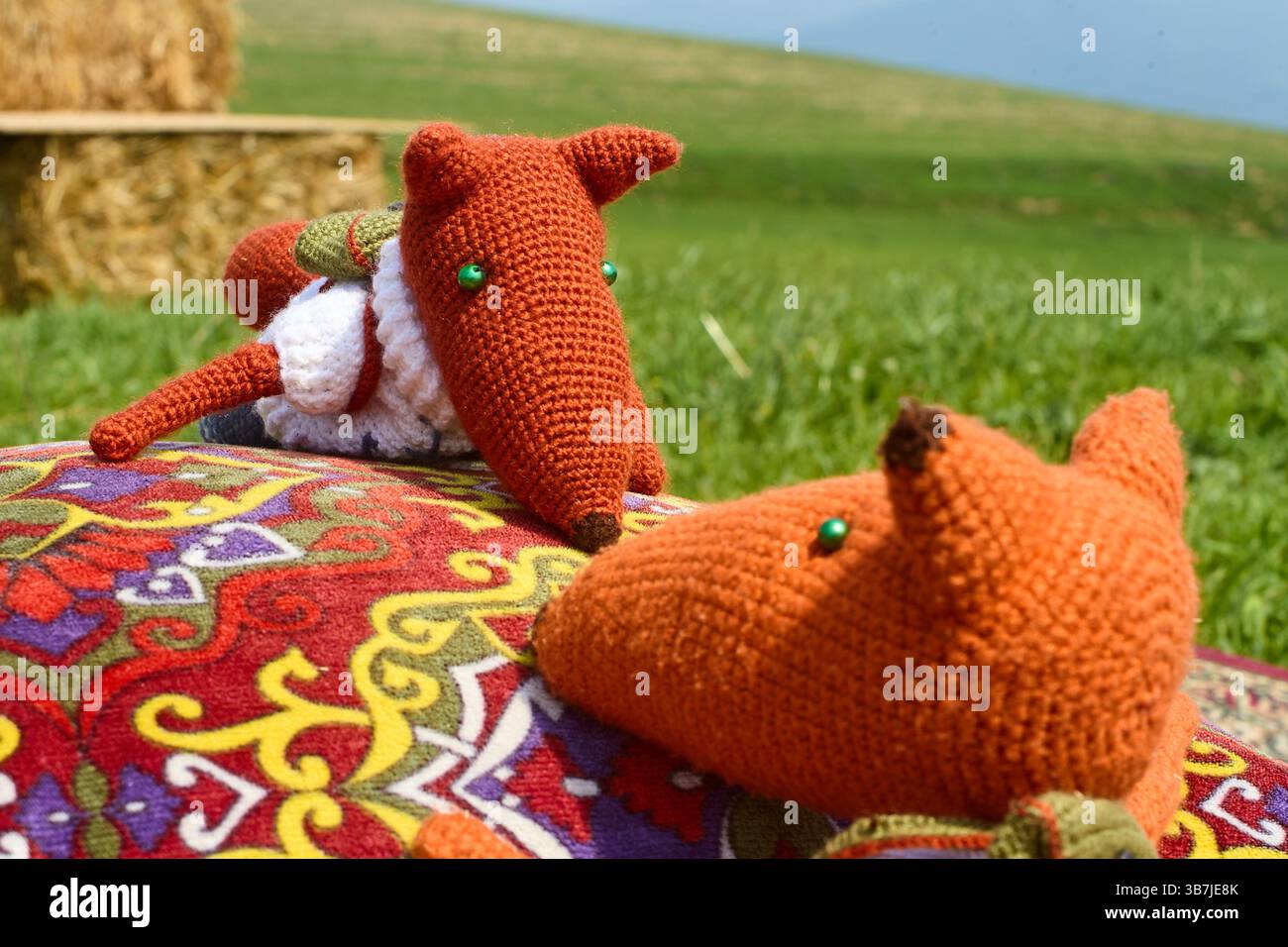 Deux jouets de renard en tricot doux, habillés de vêtements et avec des sacs à dos, blottis l'un à l'autre sur un tapis oriental coloré à côté d'un oreiller de jet, créant Banque D'Images