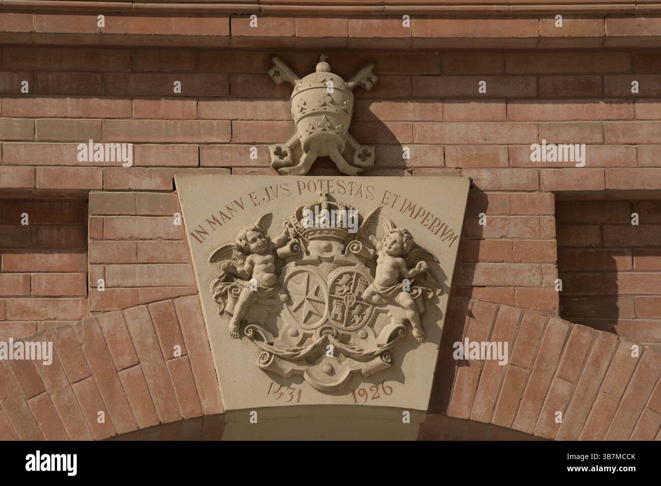 Relief en pierre d'un blason papal avec inscription latine et anges au-dessus d'une entrée en brique voûtée.Sevilla, Espagne Banque D'Images