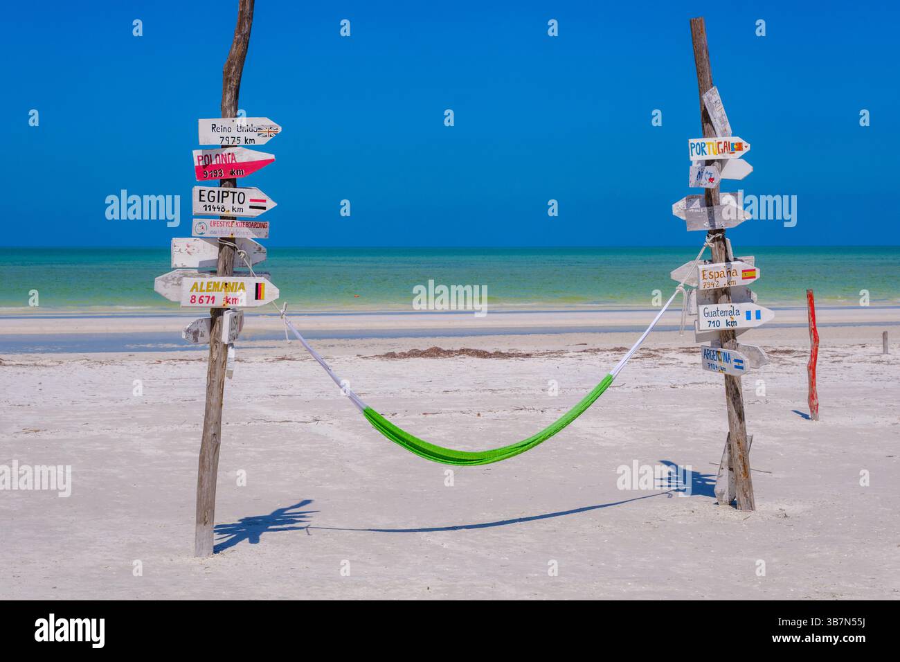 Holbox, Mexique – 10 février 2025 : un hamac vert est attaché entre deux poteaux en bois recouverts de panneaux directionnels pointant vers des pays lointains Banque D'Images Holbox, Mexique – 10 février 2025 : un hamac vert est attaché entre deux poteaux en bois recouverts de panneaux directionnels pointant vers des pays lointains Banque D'Images
