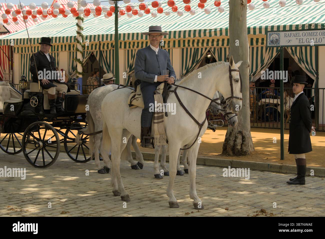 Cavalier andalou sur cheval blanc pendant la Feria de Sevilla 2025, devant des casetas rayées et des lanternes.Feria de Sevilla, Espagne Banque D'Images