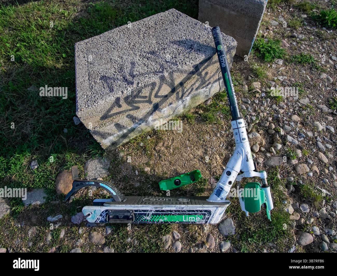 E-scooter Lime démonté abandonné à côté de blocs de béton à Berlin, symbolisant le vandalisme urbain et les problèmes de mobilité. Banque D'Images