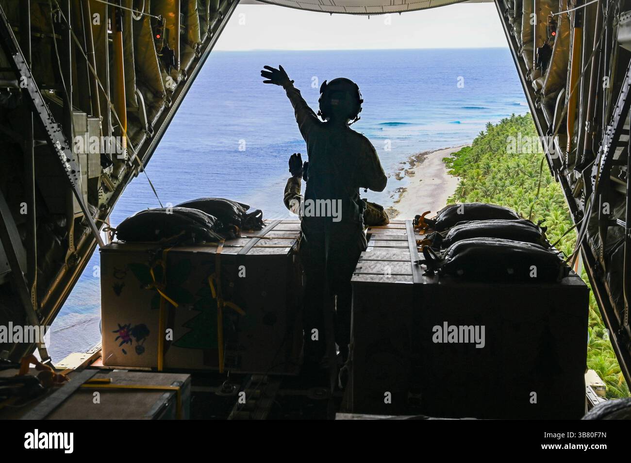 4 décembre 2023, Nama, Upper Mortlock Islands, État de Chuuk, États fédérés de Micronésie : U.S. Air Force Loadmasters SSgt. Matthew Muravez et Megan Irvin, aviateur senior, font un signe de vague alors qu'ils larguent des paquets humanitaires en parachute vers une lagune à partir d'un avion C-130J Super Hercules de l'US Air Force, lors de l'opération Christmas Drop, le 4 décembre 2023 à Nama, Îles de l'est, Micronésie. L’opération Christmas Drop est la plus ancienne mission humanitaire et de secours en cas de catastrophe, livrant 71 000 livres de nourriture, de cadeaux et de fournitures pour aider les communautés insulaires éloignées du Pacifique Sud. (Crédit image : © Sra Allison Banque D'Images