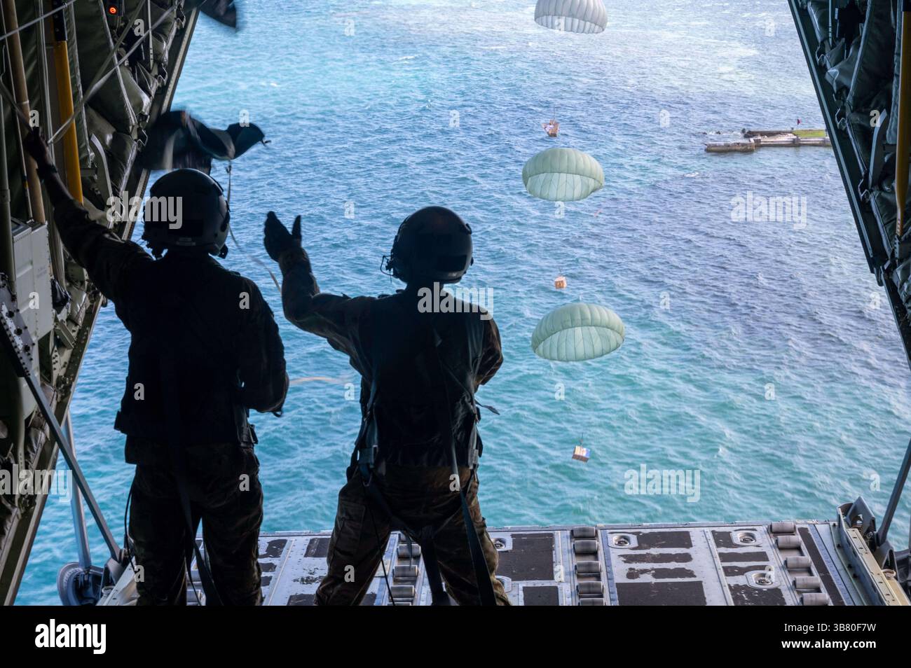 3 décembre 2023, Lukunor, îles Mortlock, État de Chuuk, États fédérés de Micronésie : les maîtres de chargement de l'US Air Force Senior Airman John Douglas, et l'aviateur Senior Ian Munoz, regardent des paquets de fret humanitaire flotter vers une lagune en parachute à partir d'un C-130J Super Hercules de l'US Air Force pendant l'opération Christmas Drop, le 3 décembre 2023 à Lukunor, Mortlock Islands, Micronésie. L’opération Christmas Drop est la plus ancienne mission humanitaire et de secours en cas de catastrophe, livrant 71 000 livres de nourriture, de cadeaux et de fournitures pour aider les communautés insulaires éloignées du Pacifique Sud. (Crédit image : © Sra Brooklyn Goli Banque D'Images