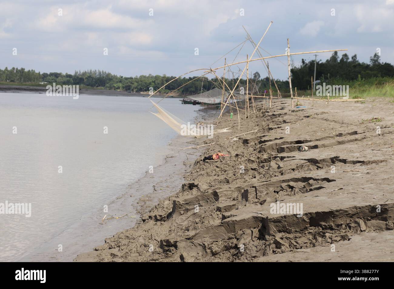 Une vue panoramique capture les rives boueuses d'une large rivière Bengali avec des structures traditionnelles de pêche en bambou et des filets, mettant en valeur le naturel et cultura Banque D'Images