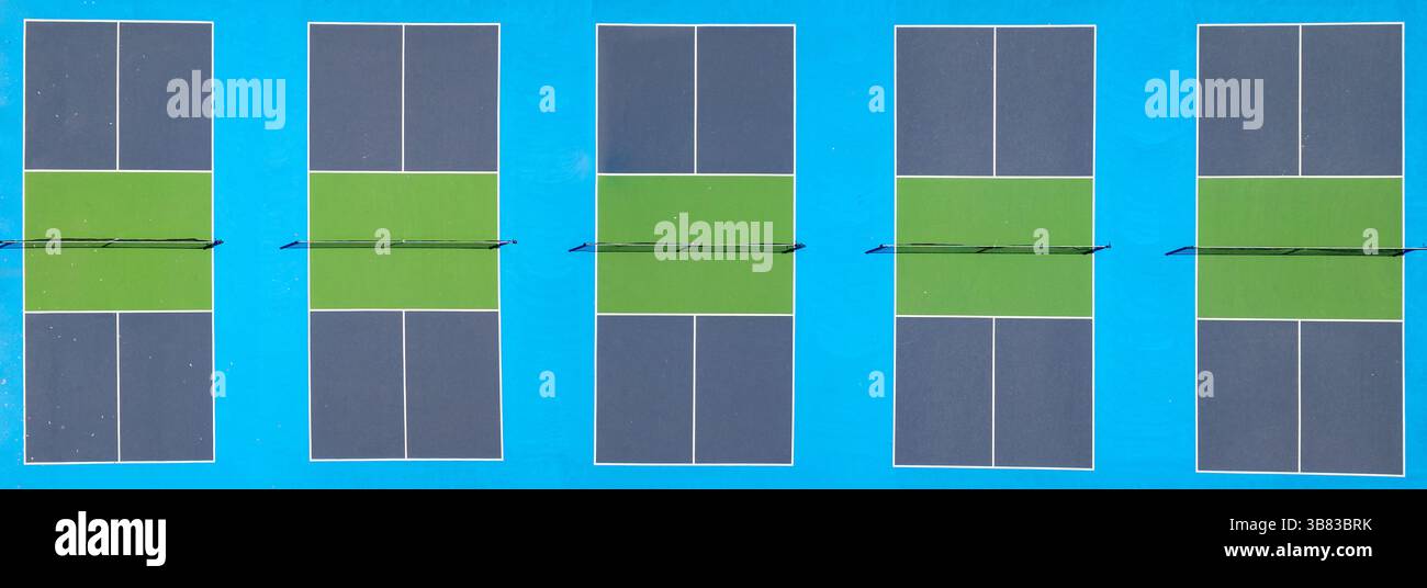Vue aérienne de haut en bas de cinq terrains de pickleball vibrants avec des aires de jeu vertes et des bordures bleues, alignés dans un motif propre et symétrique et divisés Banque D'Images