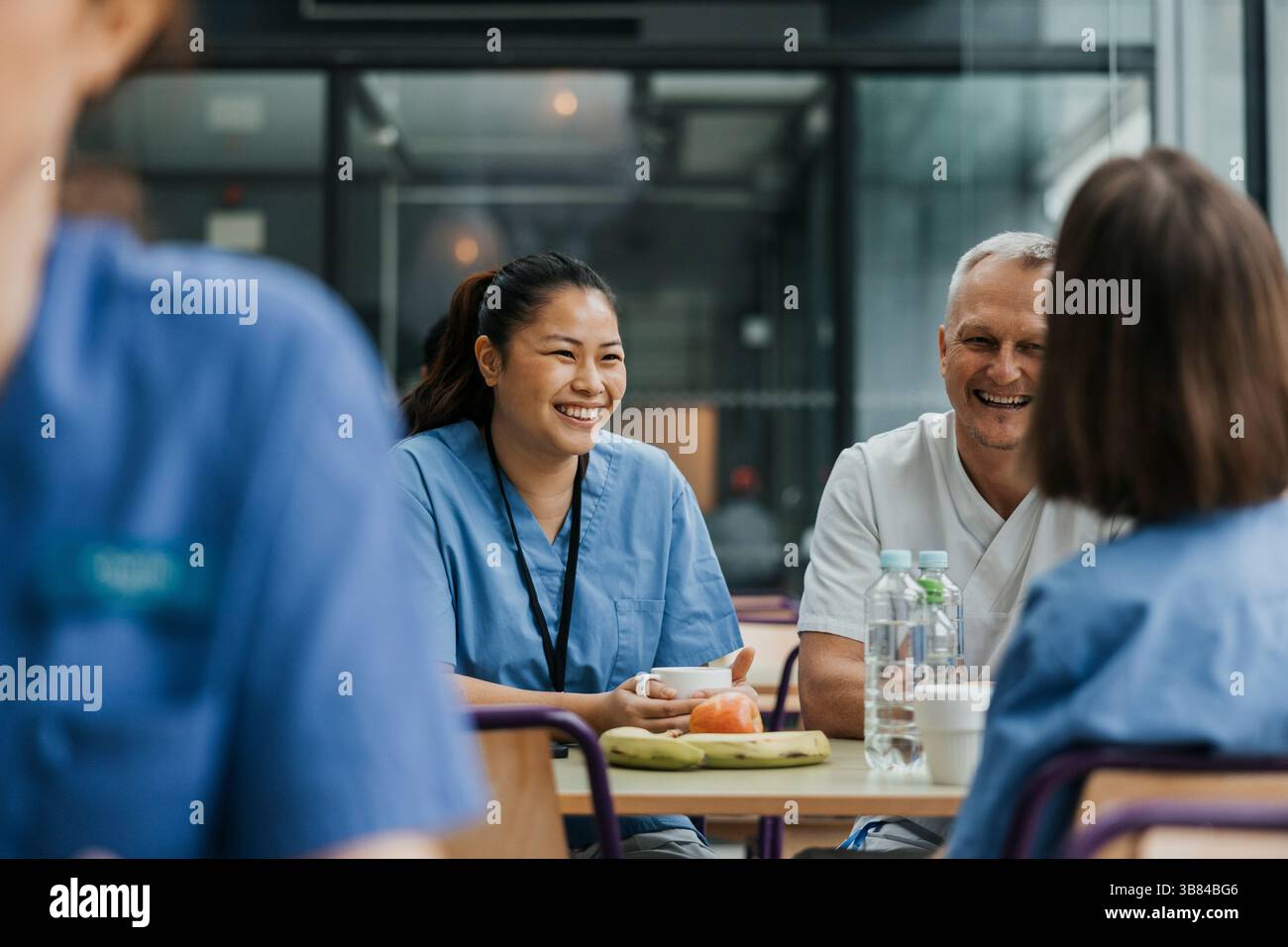 Médecin femme souriante parlant avec des collègues tout en prenant le petit déjeuner à table dans la cafétéria de l'hôpital Banque D'Images