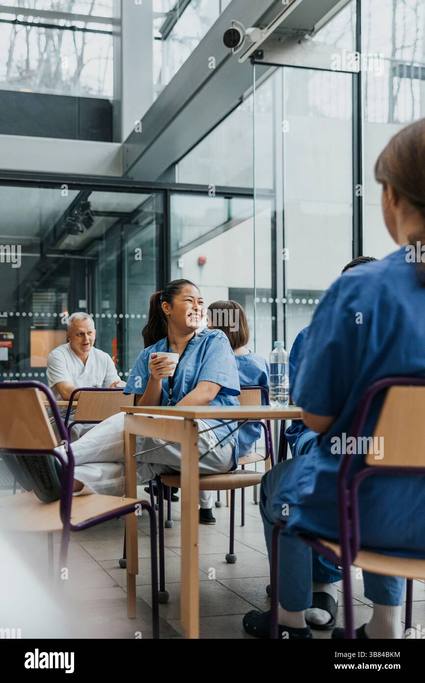 Infirmière insouciante assise sur une chaise en discutant avec des collègues à la cafétéria à l'hôpital Banque D'Images