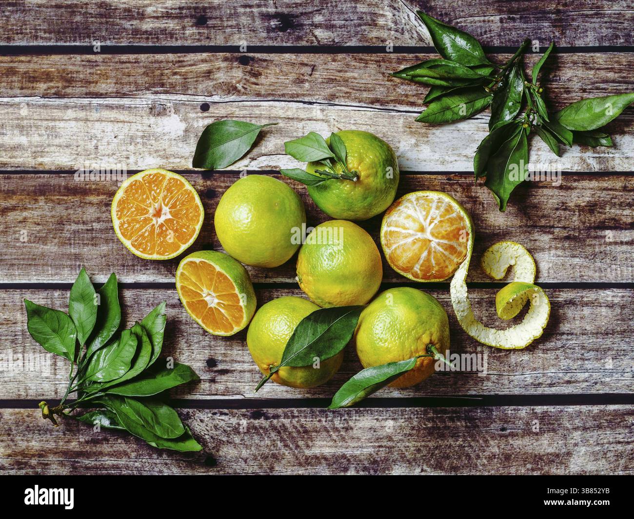 Mandarines vertes sur fond de bois ancien. Demi-mandarines fraîches et mûres, entières et pelées, avec feuilles, vue de dessus ou à plat Banque D'Images