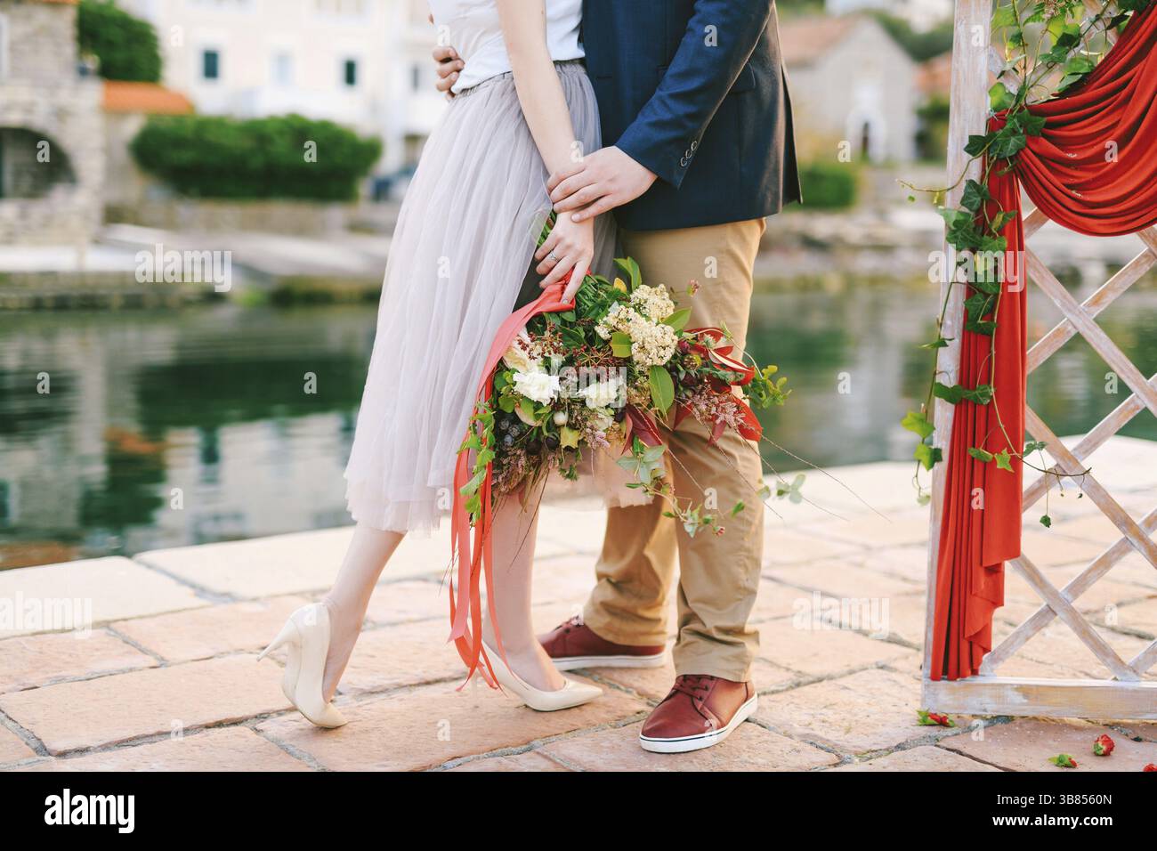 L'homme embrasse la femme avec un bouquet de fleurs dans ses mains tout en se tenant sur la jetée près d'un écran décoratif sur fond de vieilles maisons. Banque D'Images