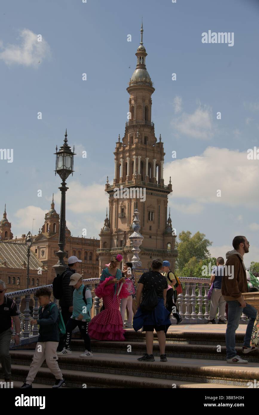 Les gens en robes de flamenco traditionnelles et les touristes marchant sur la Plaza de España pendant la Feria de Sevilla 2025, Séville, Andalucía, Espagne. Banque D'Images