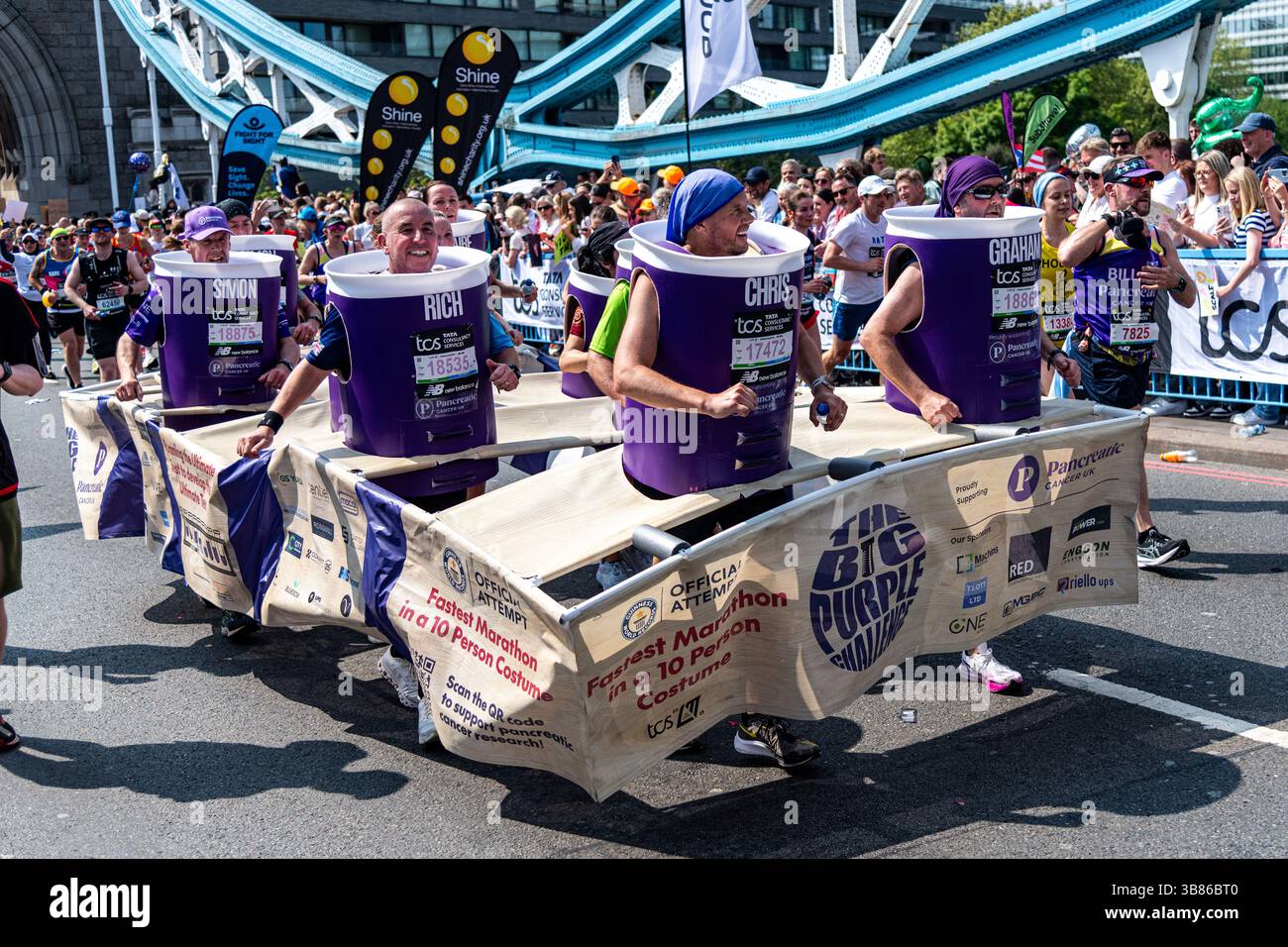 Dix personnes exécutant le Big Purple Challenge en costume de fantaisie pour le cancer du pancréas Royaume-Uni lors du marathon de Londres 2025 sur Tower Bridge, Londres, Royaume-Uni Banque D'Images