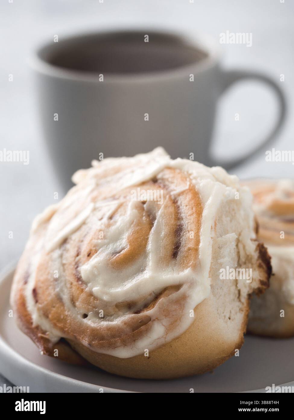 Brioches à la cannelle suédoises végétaliennes Kanelbullar avec des épices de citrouille, garniture de fromage à la crème végétalien dans une assiette avec tasse à thé sur la table. Pâtisseries idée et recette - perf Banque D'Images