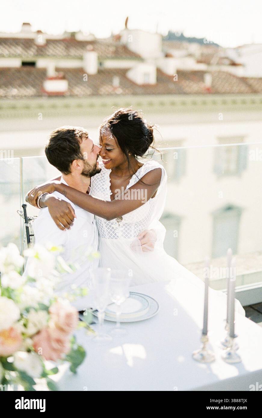 Mariée est assise dans les bras du marié à la table sur la terrasse du bâtiment. Banque D'Images