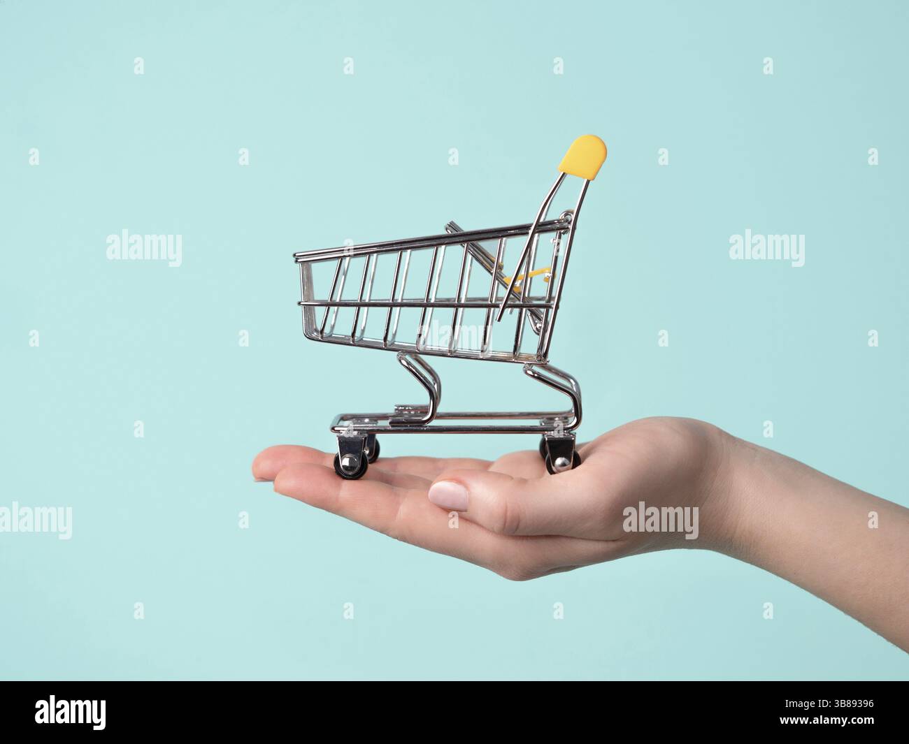 Chariot de jouet dans la main féminine.chariot à provisions sur la main sur fond bleu.Copier l'espace pour le texte ou la conception.magasin chariot modèle sans couture comme vente, di Banque D'Images