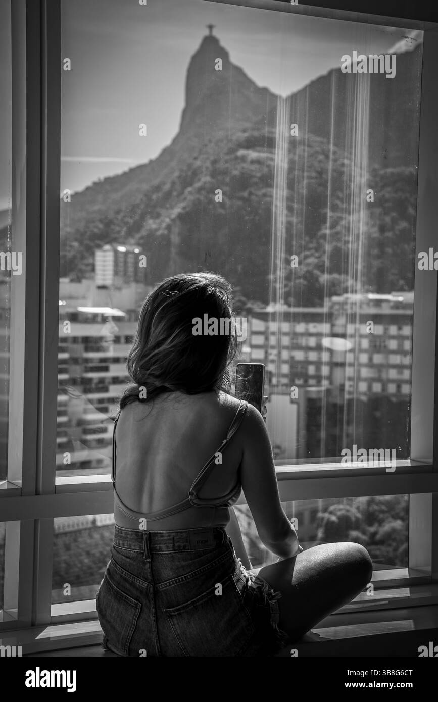 Femme assise près de la fenêtre avec vue du Christ Rédempteur - Rio de Janeiro, Brésil Banque D'Images