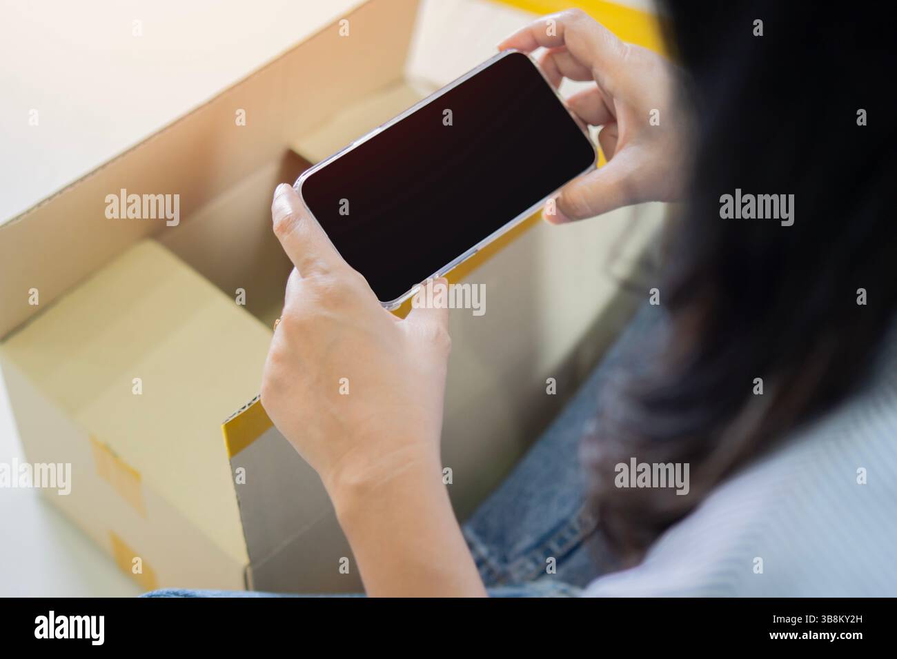 Vue arrière de la femme tenant l'écran maquette de téléphone et prendre une photo de l'ordre de livraison de boîte d'expédition commerciale sur smartphone. Copier l'espace. Banque D'Images