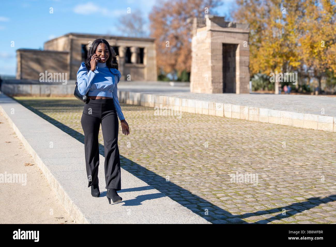 Élégante femme d'affaires marchant et parlant au téléphone dans le parque del oeste, près du temple de debod à madrid, en espagne, pendant une journée d'automne ensoleillée Banque D'Images