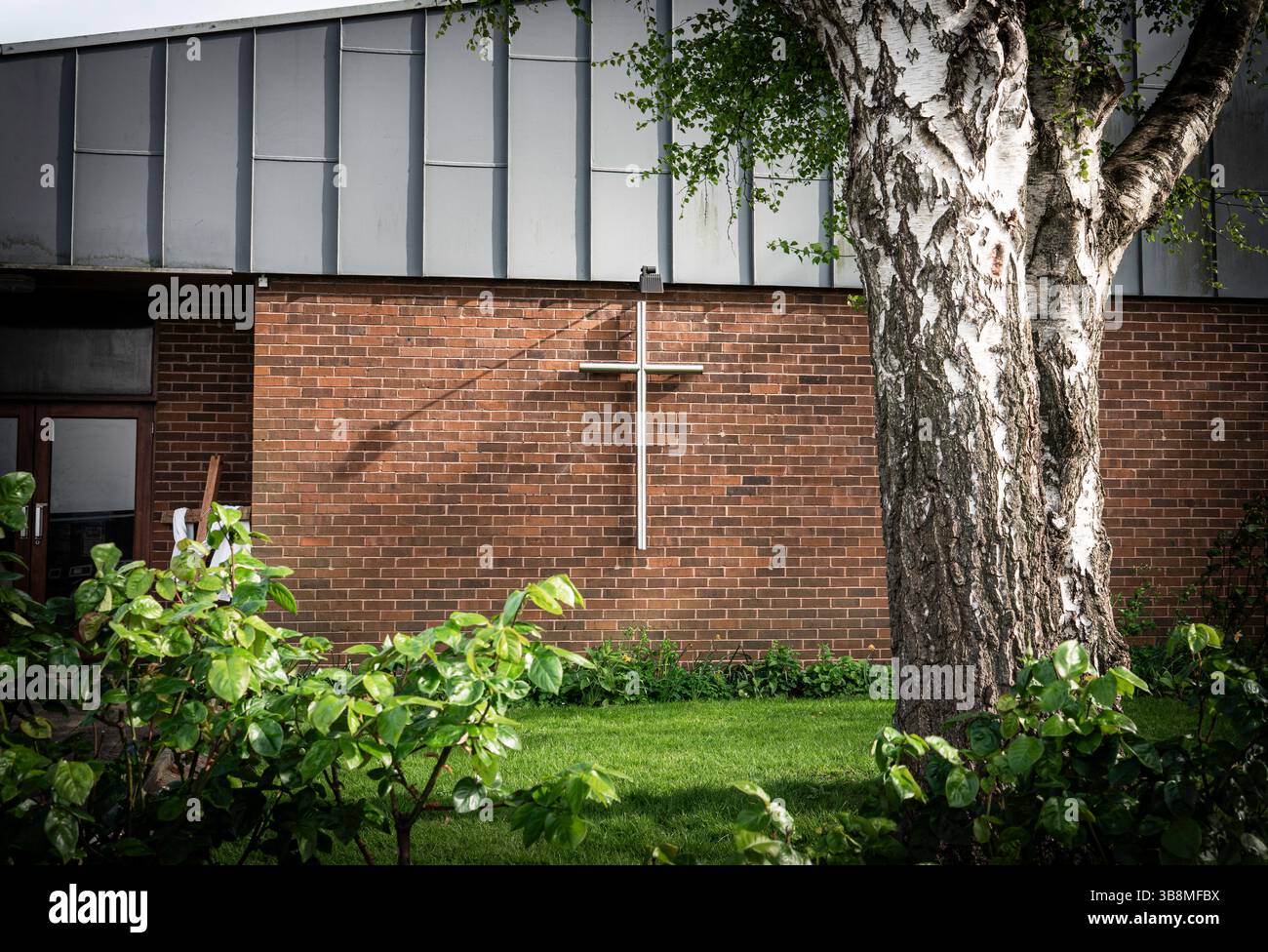 Église Sainte avec une grande croix chrétienne contre un mur de briques et un arbre à côté de son jardin Banque D'Images