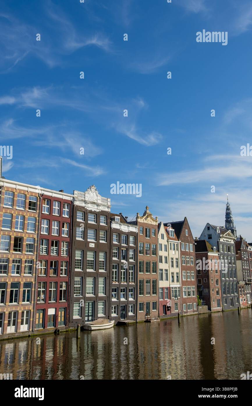Les maisons de canal d'Amsterdam sont hautes, reflétant dans l'eau. Les touristes admirent l'architecture, capturant le charme de la ville. Banque D'Images