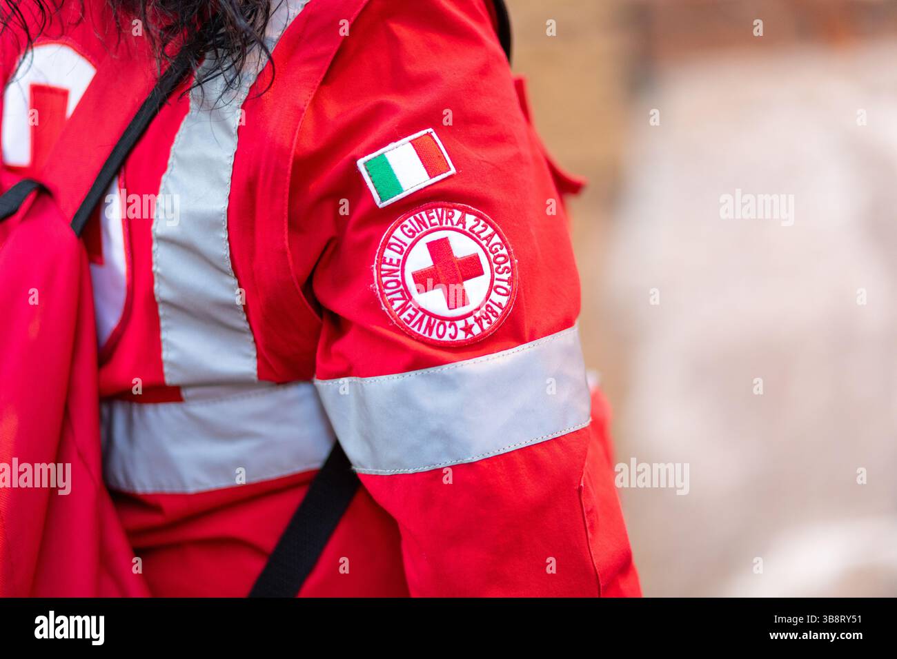 Rome, Italie - 18 avril 2025 : vue rapprochée de la manche sur l'uniforme rouge d'un ambulancier paramédical de la Croix-Rouge italienne, avec un badge représentant la Convention de Genève aux côtés du drapeau italien, symbolisant le service humanitaire Banque D'Images