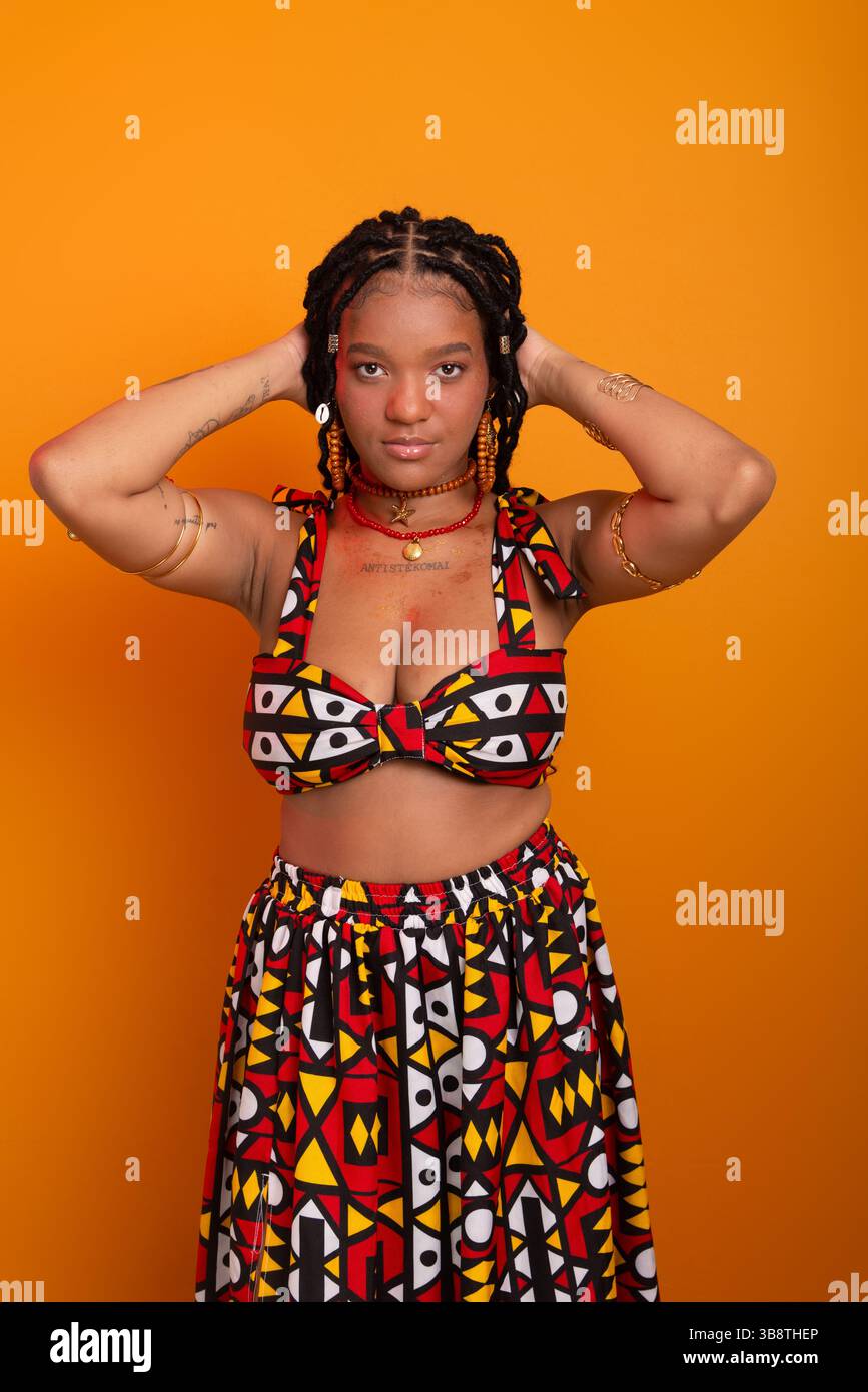 Belle jeune femme avec des tresses dans les cheveux, debout, portant des vêtements traditionnels, posant pour la caméra. Isolé sur fond couleur moutarde. Banque D'Images Belle jeune femme avec des tresses dans les cheveux, debout, portant des vêtements traditionnels, posant pour la caméra. Isolé sur fond couleur moutarde. Banque D'Images