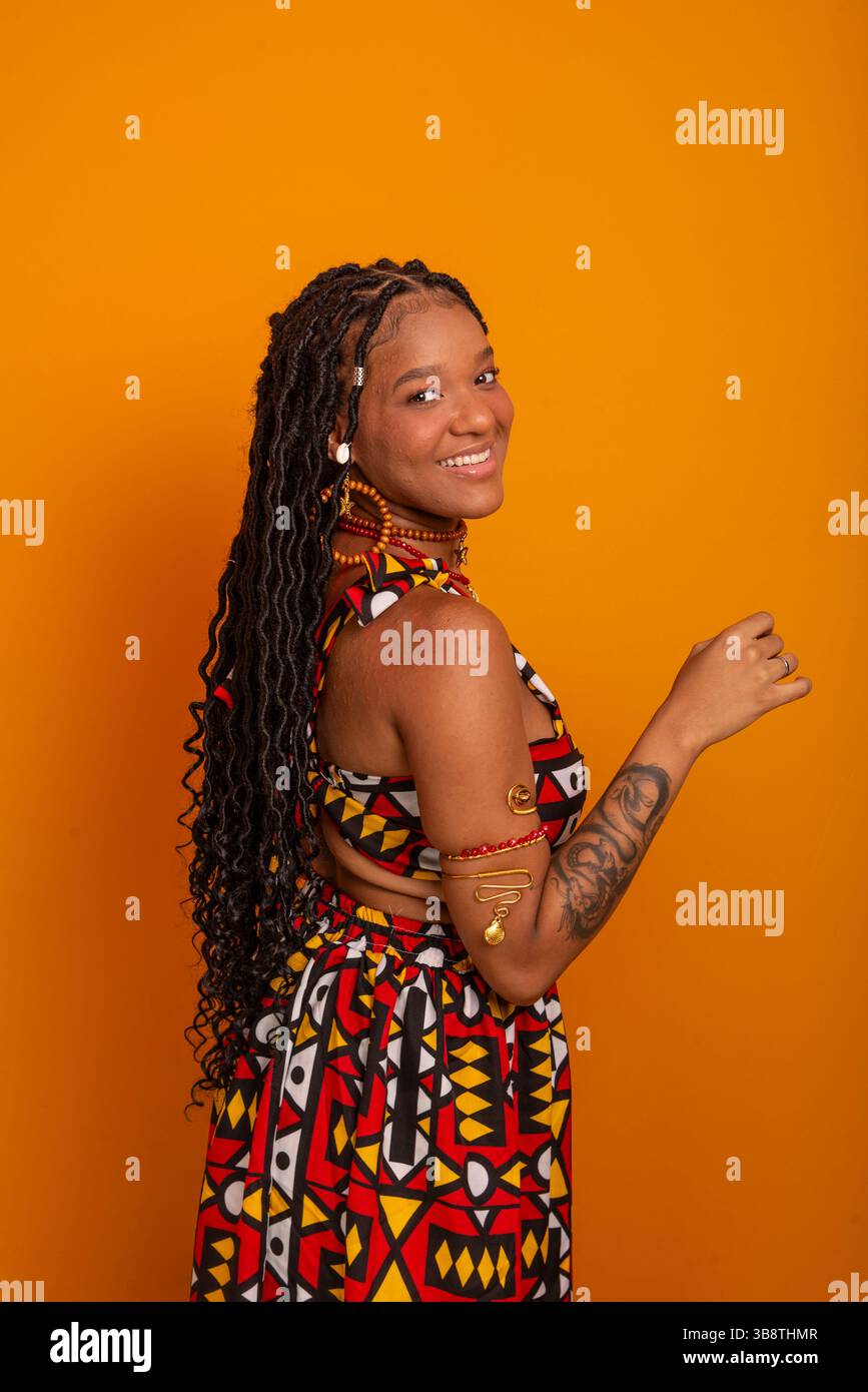 Belle jeune femme avec des tresses dans les cheveux, debout, portant des vêtements traditionnels, posant pour la caméra. Isolé sur fond couleur moutarde. Banque D'Images Belle jeune femme avec des tresses dans les cheveux, debout, portant des vêtements traditionnels, posant pour la caméra. Isolé sur fond couleur moutarde. Banque D'Images