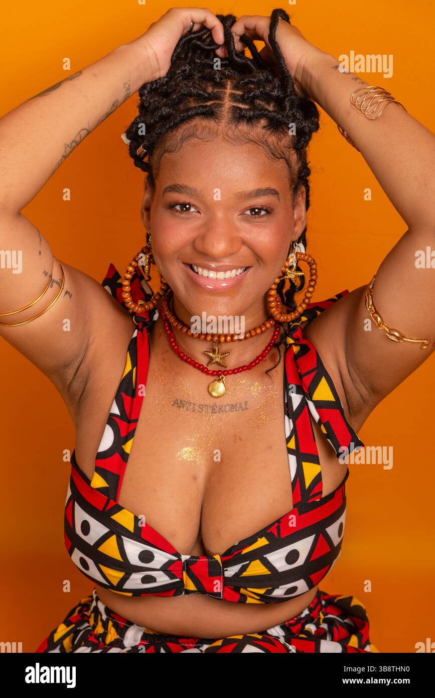 Belle jeune femme assise avec des tresses dans ses cheveux portant des vêtements traditionnels, posant pour la caméra. Isolé sur fond de couleur moutarde. CON Banque D'Images Belle jeune femme assise avec des tresses dans ses cheveux portant des vêtements traditionnels, posant pour la caméra. Isolé sur fond de couleur moutarde. CON Banque D'Images
