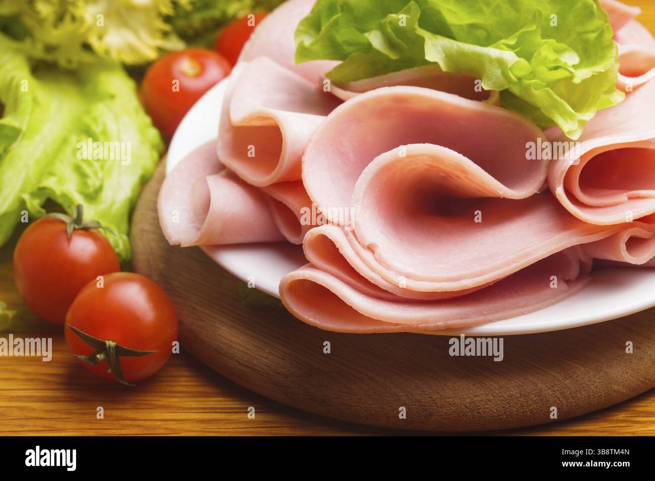 Tranches de jambon frais avec lattuce et tomate cerise sur la planche de bois Banque D'Images Tranches de jambon frais avec lattuce et tomate cerise sur la planche de bois Banque D'Images