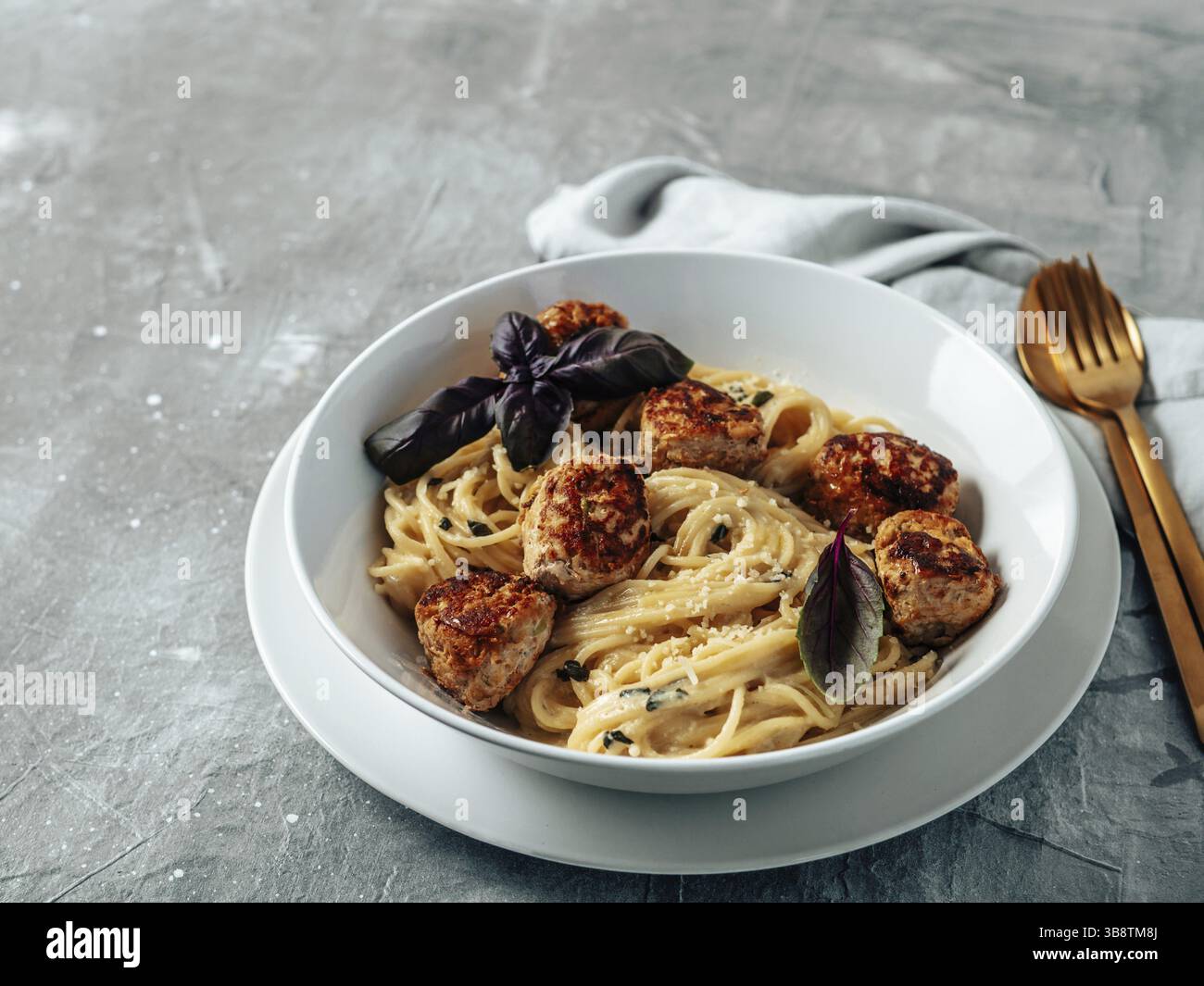 Boulettes de parmesan de courgettes aux pâtes Carbonara dans une assiette blanche sur fond gris. Vue rapprochée de la carbonara crémeuse avec espace de copie restant Banque D'Images